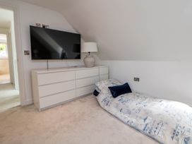 A bedroom with a low bed near a white dresser with a lamp and a wall mounted television at Buzzards View in Dyserth