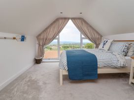 A bedroom with a bed covered by striped bedding and a blue throw in front of a large window with curtains overlooking fields at Buzzards View in Dyserth