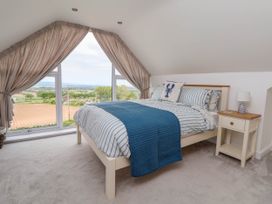 A bedroom with a bed next to a nightstand and large windows with curtains at Buzzards View in Dyserth