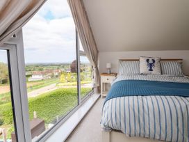 A bedroom with a striped bed and a nightstand next to a large window with a view of greenery and houses at Buzzards View in Dyserth