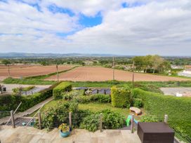 A garden with plants and a patio overlooking fields and distant hills at Buzzards View in Dyserth