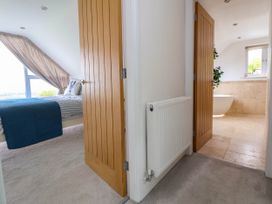 A view of a hallway with two open wooden doors leading to a bedroom with a bed and a bathroom with a bathtub at Buzzards View in Dyserth