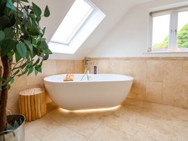 A bathroom with a freestanding bathtub under a skylight next to a wooden stool and a plant at Buzzards View in Dyserth