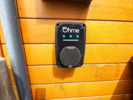 A black Ohme electric vehicle charger mounted on a wooden wall with a grey pipe running beside it at Buzzards View in Dyserth
