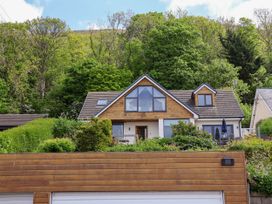 A house with a wooden garage door and large windows surrounded by bushes and trees at Buzzards View in Dyserth