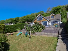 A backyard with a swing set slide and garden toys in front of a house with a patio and stairs at Buzzards View in Dyserth