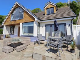 An outdoor patio area with chairs tables and umbrella outside a house with large windows at Buzzards View in Dyserth