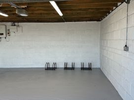 An empty room with white painted brick walls a gray floor ceiling with exposed wooden beams and three black metal bike racks attached to a wall at Buzzards View in Dyserth