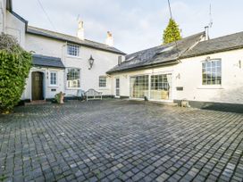 A paved courtyard with a bench and a white house with multiple windows at The Coach House in Abergavenny