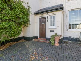 A paved entrance with a wooden door and a small window next to it with a large plant in a pot and ivy growing on the wall at The Coach House in Abergavenny