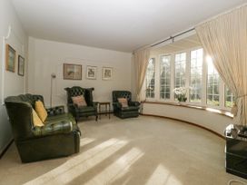 A living room with green leather armchairs and sofa by windows with curtains at The Coach House in Abergavenny