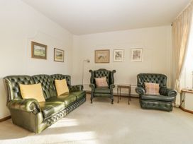 A living room with green leather sofa and armchairs with cushions and framed paintings on the wall at The Coach House in Abergavenny