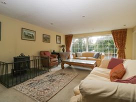 A living room with sofas, armchair, glass coffee table, fireplace with guard, rug, paintings, and large window with curtains at The Coach House in Abergavenny