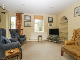 A living room with armchairs a television on a glass stand and framed pictures on the wall at The Coach House in Abergavenny