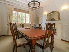 A dining room with a wooden table and six chairs a large window with curtains and a wall mirror at The Coach House in Abergavenny