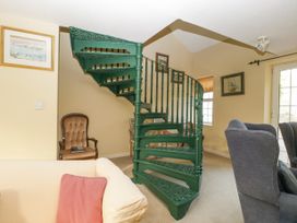 A room with a green spiral staircase a beige sofa with a red cushion a brown armchair and gray chairs at The Coach House in Abergavenny