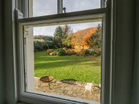 A garden with green grass trees a white chair and a fire pit viewed through a window at The Coach House in Abergavenny