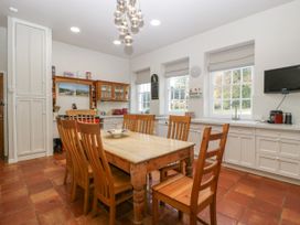 A dining area with a wooden table and chairs in a kitchen with white cabinets and large windows at The Coach House in Abergavenny