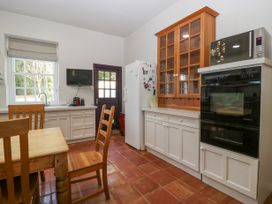A kitchen with wooden chairs a dining table white cabinets a refrigerator and a wall-mounted television at The Coach House in Abergavenny