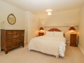 A bedroom with a bed two bedside tables with lamps a wooden chest of drawers and a round mirror at The Coach House in Abergavenny