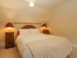 A bedroom with a bed with two pillows and a beige blanket two nightstands with lamps and a ceiling light at The Coach House in Abergavenny