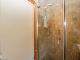 A shower enclosure with a glass door and tiled walls next to a white door at The Coach House in Abergavenny