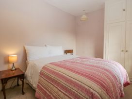 A bedroom with a bed covered by a striped pink and beige quilt a wooden nightstand with a lamp a wooden chair and built in white wardrobes at The Coach House in Abergavenny