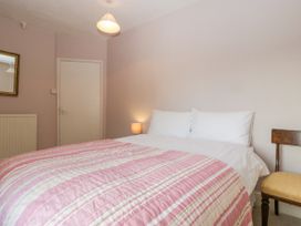 A bedroom with a double bed with pink striped bedding a wooden chair a small lamp a mirror and a door at The Coach House in Abergavenny
