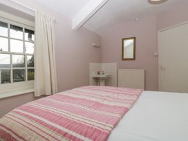 A bedroom with a bed covered with a pink striped blanket a window with cream curtains a sink a mirror and a radiator at The Coach House in Abergavenny