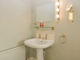 A bathroom sink with two taps a mirror and a glass shelf with hand wash at The Coach House in Abergavenny