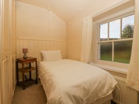 A small bedroom with a single bed bedside table lamp and a window with curtains at The Coach House in Abergavenny
