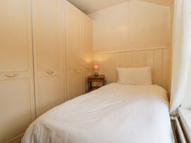 A small bedroom with a single bed white bedding a wooden nightstand with a lamp and built in wardrobes at The Coach House in Abergavenny