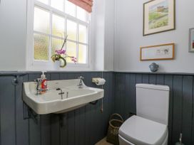 A bathroom with a white sink and toilet a window with a red blind and framed pictures on the wall at The Coach House in Abergavenny