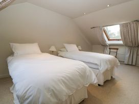 A bedroom with two single beds two white bedside lamps a chair and a window with curtains at The Coach House in Abergavenny