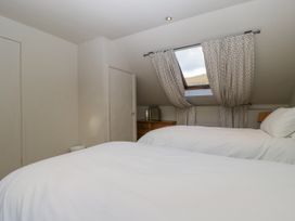 A bedroom with two beds covered in white linens a window with curtains and a wooden dresser at The Coach House in Abergavenny