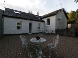 An outdoor patio area with two sets of metal tables and chairs in front of a white stone house at The Coach House in Abergavenny