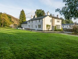 A large white house with multiple chimneys surrounded by a green lawn and trees at The Coach House in Abergavenny