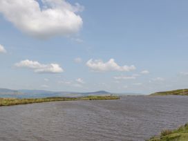 A lake with grass on the shore and hills in the distance under a cloudy sky at The Coach House in Abergavenny