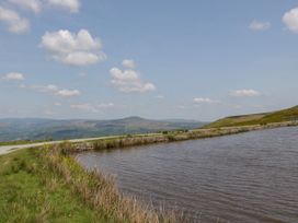 A body of water next to a dirt path with grass and hills in the background at The Coach House in Abergavenny