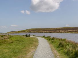 A gravel path along a river with a bench and a trash bin under a partly cloudy sky