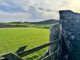 A wooden gate and stone wall opening to green fields with hills under a cloudy sky at Old Cottage in Oxen Park near Ulverston