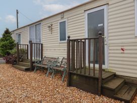A beige mobile home with two small wooden porches and a wooden bench on gravel at Willebby in South Chard