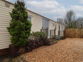 A mobile home with two sets of wooden steps and benches on a gravel ground with trees and a wooden fence in the background at Willebby South Chard