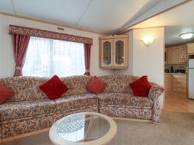 A living area with a patterned corner sofa and red cushions near a window with red curtains and a glass top coffee table at Willebby in South Chard