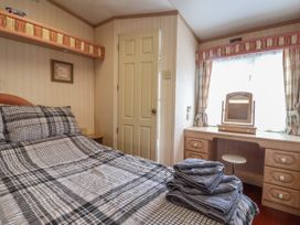 A bedroom with a bed covered in plaid bedding and folded towels a door a vanity with a mirror and stool under a window with curtains at Willebby in South Chard