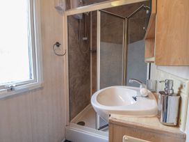 A bathroom with a corner shower enclosure a white sink with a faucet and a soap dispenser a glass holder a towel ring and a window at Willebby in South Chard