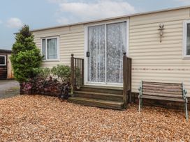 A mobile home with a sliding glass door with lace curtains a small wooden porch wooden bench gravel ground and some shrubs at Willebby in South Chard