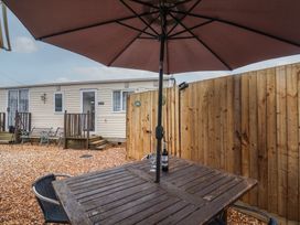 An outdoor seating area with a wooden table under a large umbrella and a bottle of wine with glasses in front of a fenced area and a beige caravan at Willebby in South Chard