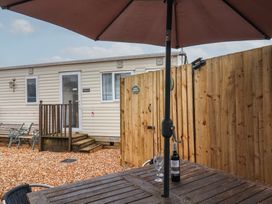 An outdoor area with a wooden table and umbrella a bottle of wine and wine glasses near a wooden fence and a beige mobile home at Willebby in South Chard