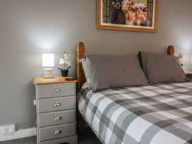 A bedroom with a bed covered in gray and white checkered bedding two gray pillows bedside tables each with a lamp and a small flower pot and a framed picture of cows on the wall at Bobby's Lodge in South Chard